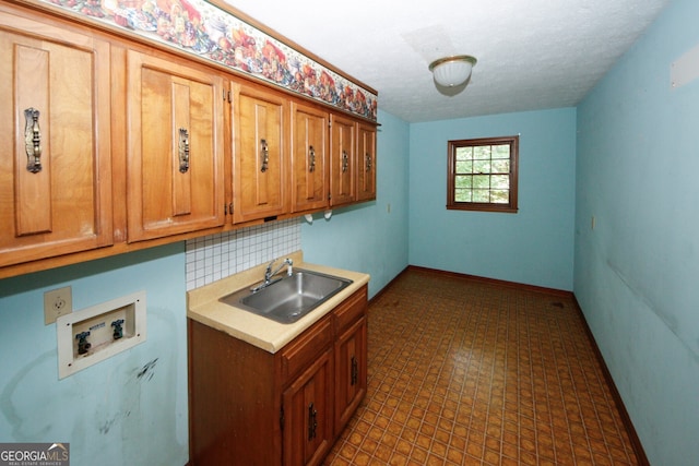 laundry room featuring a textured ceiling, hookup for a washing machine, a sink, baseboards, and cabinet space