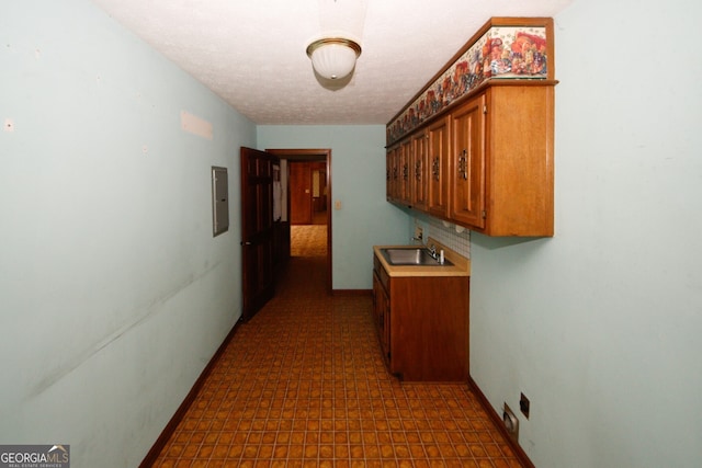 hall featuring dark floors, electric panel, a sink, and baseboards