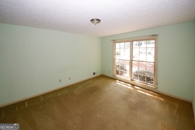 carpeted spare room featuring a textured ceiling, visible vents, and baseboards