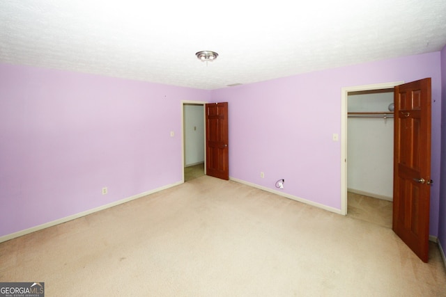 unfurnished bedroom featuring baseboards, light colored carpet, a spacious closet, a textured ceiling, and a closet