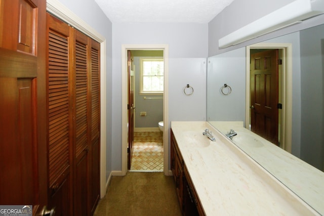 bathroom with baseboards, toilet, a textured ceiling, vanity, and a closet