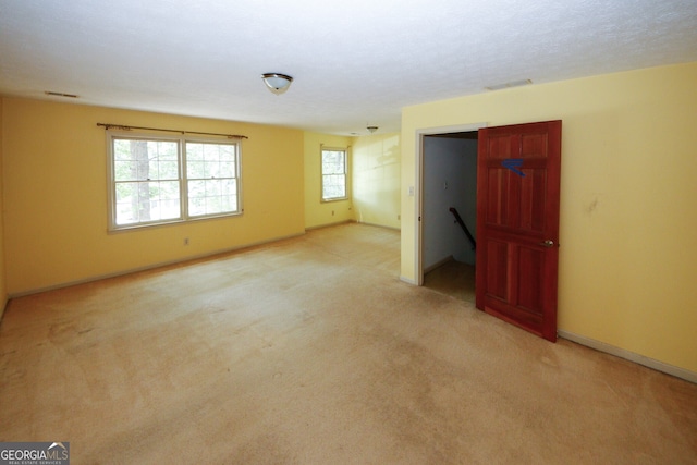 unfurnished bedroom featuring light carpet, a textured ceiling, visible vents, and baseboards