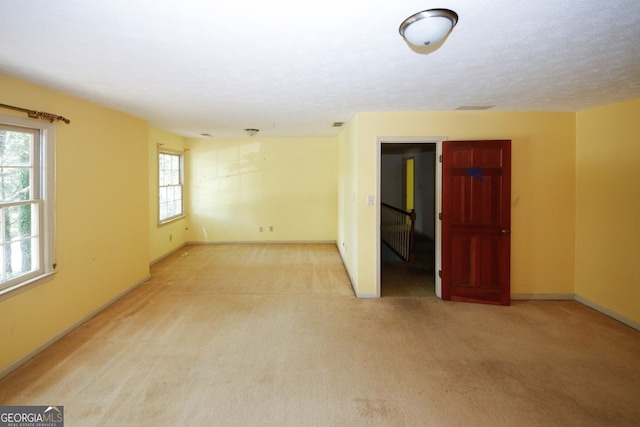 unfurnished room with light carpet, a textured ceiling, and baseboards