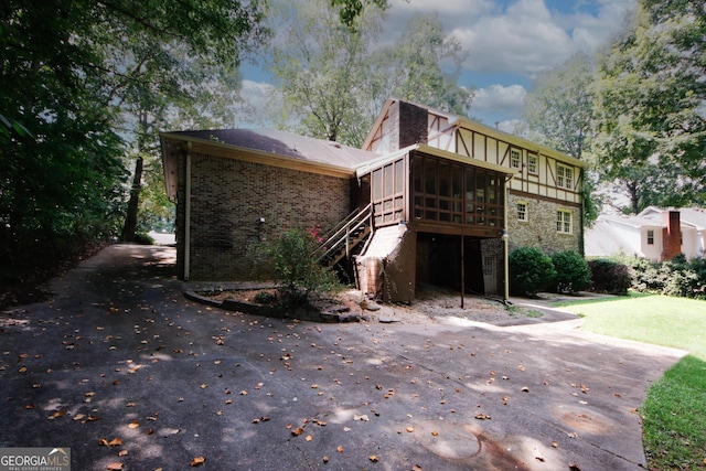 exterior space featuring brick siding, a sunroom, driveway, stone siding, and stairway