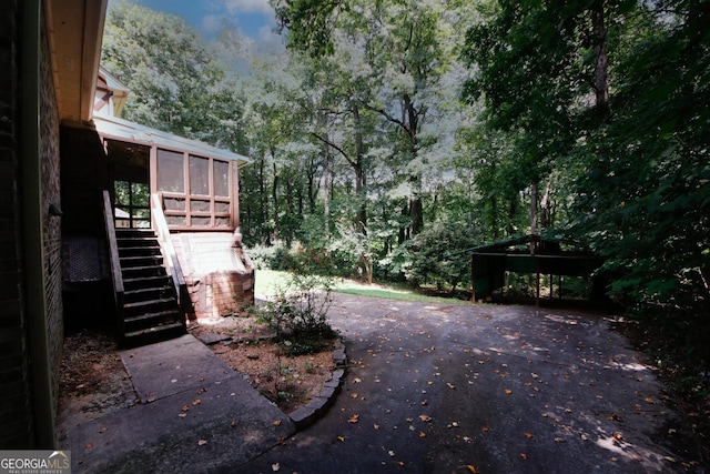 view of yard featuring aphalt driveway, stairway, and a sunroom