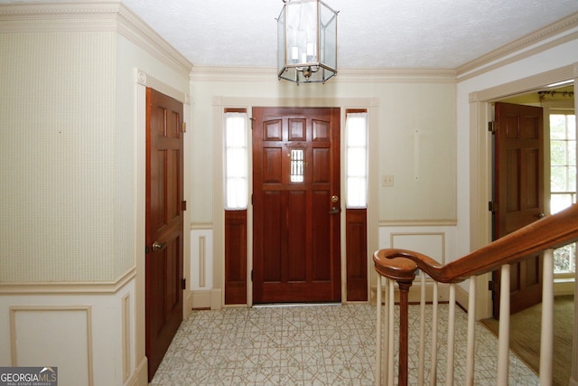 foyer entrance with a wainscoted wall, crown molding, stairway, and a decorative wall