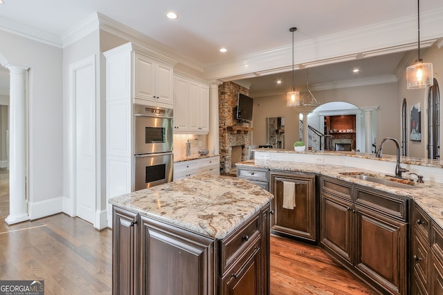 kitchen with a stone fireplace, hardwood / wood-style floors, white cabinetry, sink, and double oven