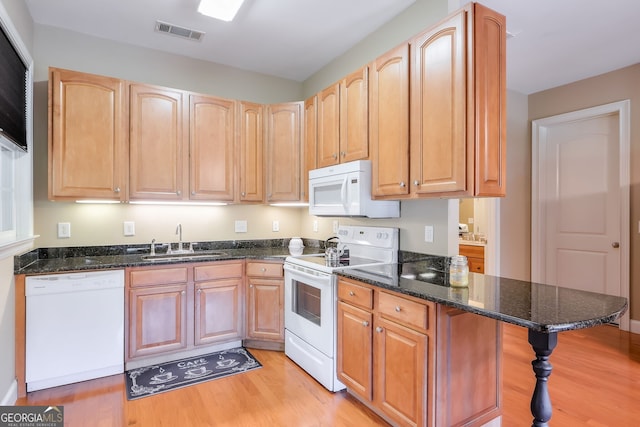 kitchen with dark stone counters, a kitchen bar, light hardwood / wood-style floors, sink, and white appliances