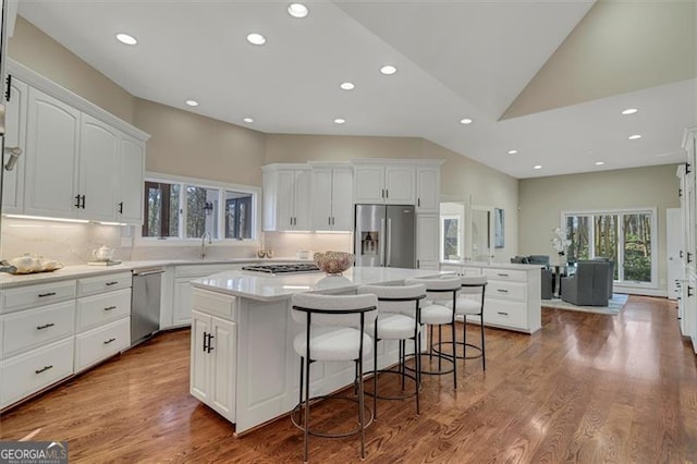 kitchen with white cabinets, high vaulted ceiling, a kitchen island, and appliances with stainless steel finishes