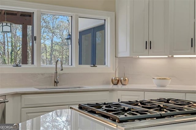 kitchen featuring light stone countertops, range, white cabinetry, and sink