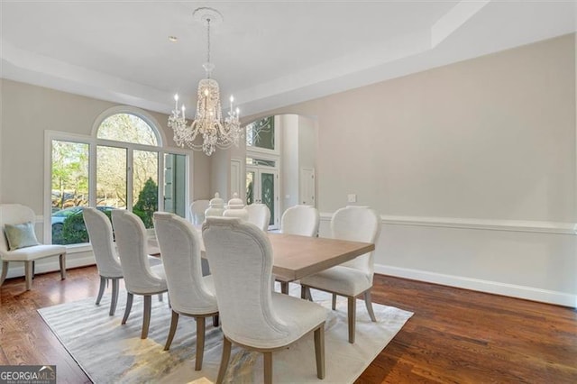 dining space featuring a tray ceiling, an inviting chandelier, and dark hardwood / wood-style floors