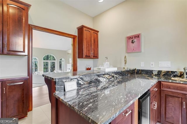 kitchen with dark stone countertops, kitchen peninsula, sink, and beverage cooler