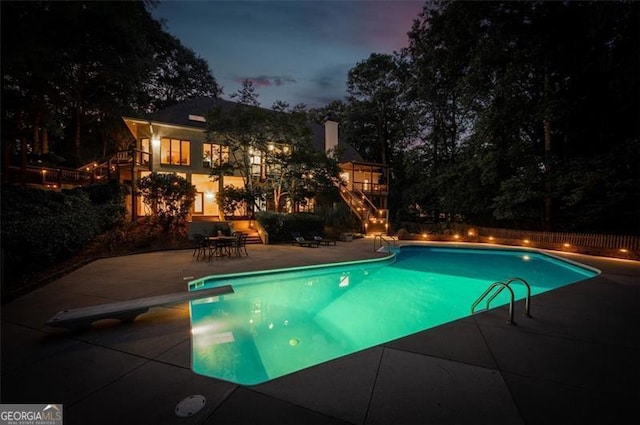 pool at dusk featuring a diving board and a patio area