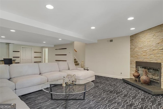 living room with a stone fireplace and dark colored carpet