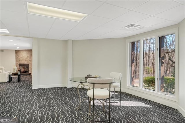 carpeted dining room with a fireplace, a drop ceiling, and plenty of natural light