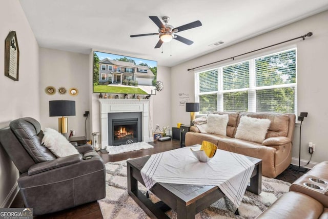 living area with visible vents, dark wood-type flooring, a ceiling fan, a lit fireplace, and baseboards