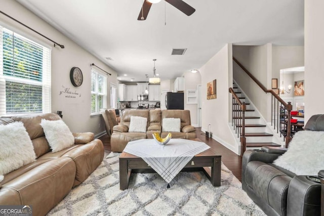 living area with stairs, visible vents, wood finished floors, baseboards, and ceiling fan with notable chandelier