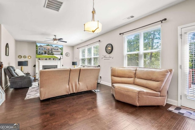 living area with dark wood-style flooring, a fireplace, visible vents, and baseboards