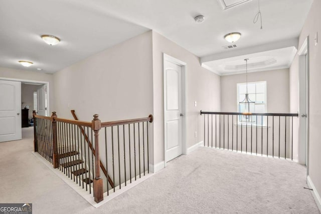 hallway featuring light carpet, an upstairs landing, visible vents, a raised ceiling, and attic access