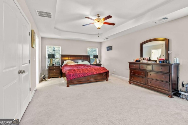 bedroom with a tray ceiling, visible vents, light carpet, and baseboards