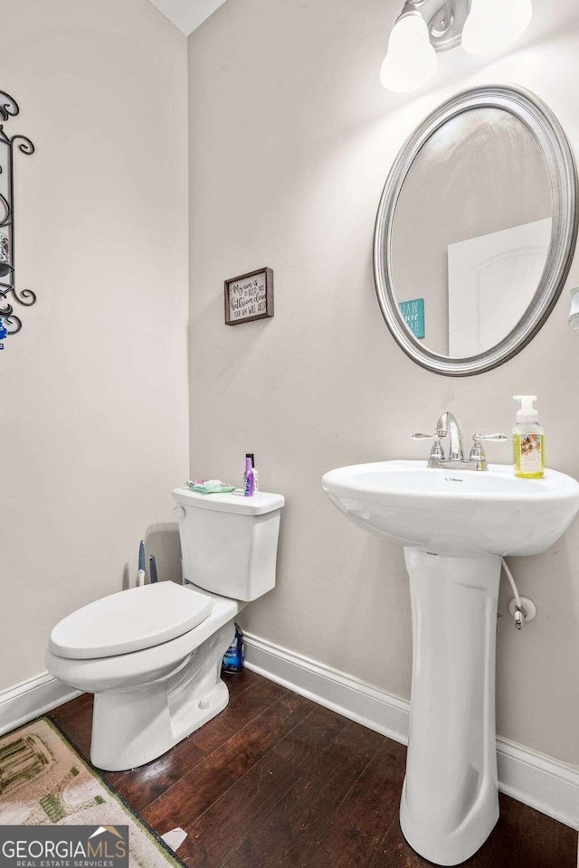 half bathroom featuring a sink, toilet, baseboards, and wood finished floors