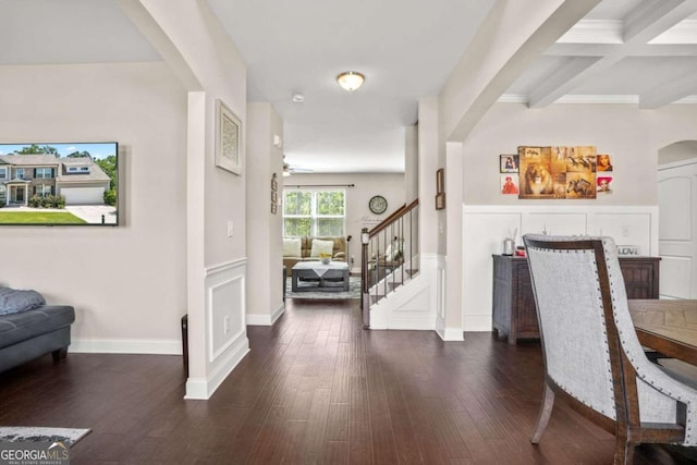 foyer entrance with dark wood-style floors, arched walkways, a decorative wall, beamed ceiling, and stairs