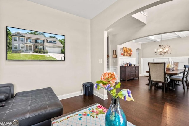 living room with arched walkways, dark wood finished floors, an inviting chandelier, beamed ceiling, and baseboards