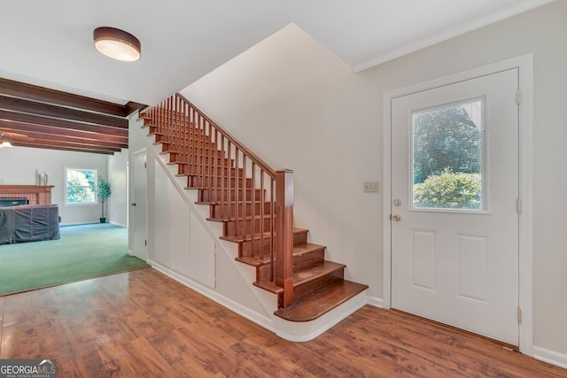 carpeted entryway featuring beam ceiling and a brick fireplace