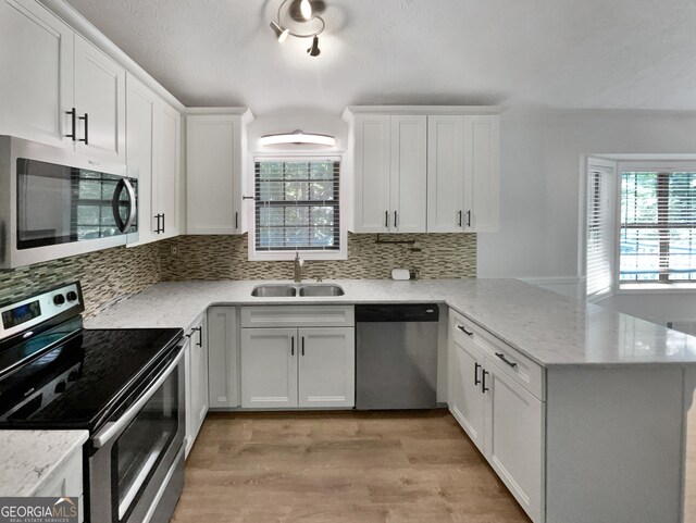 kitchen with appliances with stainless steel finishes, light hardwood / wood-style floors, tasteful backsplash, sink, and kitchen peninsula