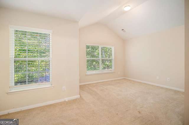 spare room with vaulted ceiling, baseboards, visible vents, and light colored carpet