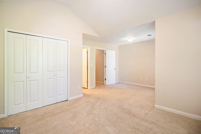 unfurnished bedroom featuring vaulted ceiling, a closet, baseboards, and light colored carpet