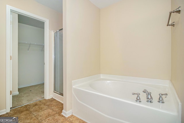 full bathroom featuring tile patterned flooring, a garden tub, baseboards, a spacious closet, and a shower stall