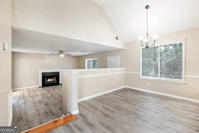 empty room with ceiling fan with notable chandelier, high vaulted ceiling, and wood-type flooring