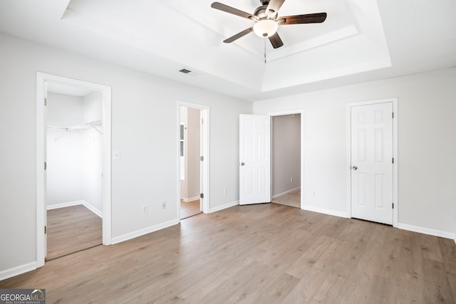 unfurnished bedroom with ceiling fan, a raised ceiling, light wood-type flooring, and ensuite bathroom