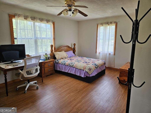 bedroom with multiple windows, wood-type flooring, a textured ceiling, and ceiling fan