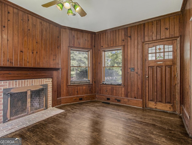 unfurnished living room with dark wood-type flooring, crown molding, wooden walls, a brick fireplace, and ceiling fan