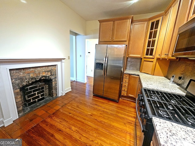 kitchen featuring decorative backsplash, light stone countertops, stainless steel appliances, and wood-type flooring