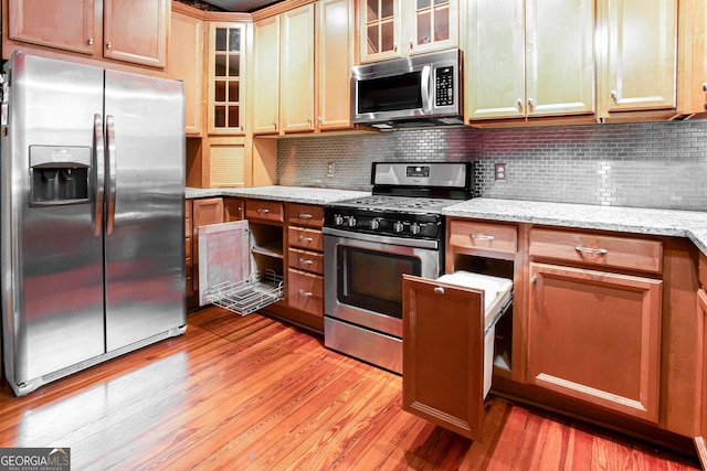 kitchen featuring appliances with stainless steel finishes, light hardwood / wood-style floors, tasteful backsplash, and light stone countertops