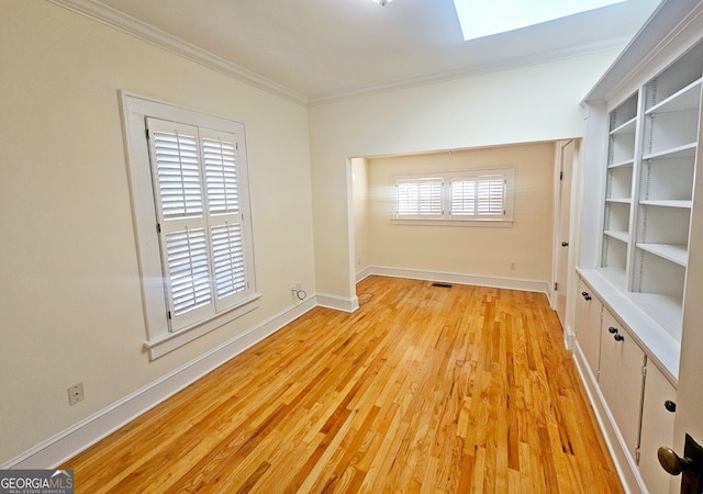 empty room with light wood-type flooring, a skylight, and crown molding