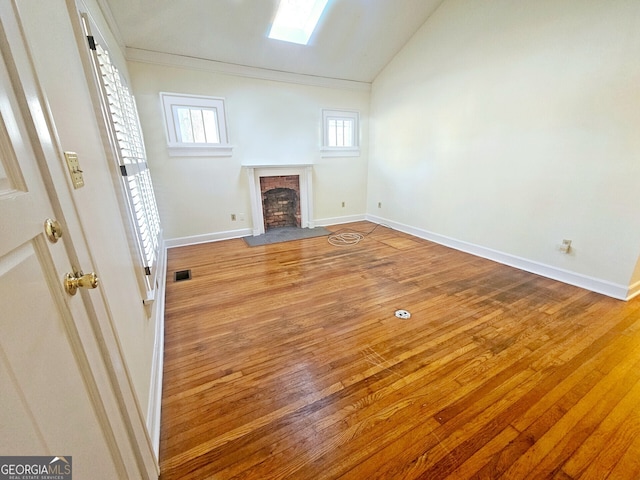 unfurnished living room with lofted ceiling with skylight, light hardwood / wood-style floors, and a brick fireplace