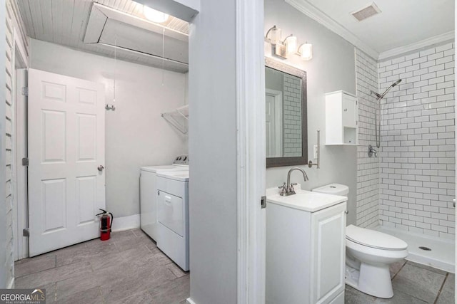 bathroom featuring tiled shower, toilet, washer and dryer, ornamental molding, and vanity