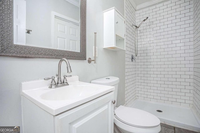 bathroom with crown molding, a tile shower, vanity, and toilet