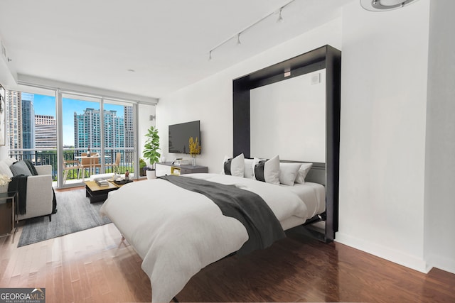 bedroom with wood-type flooring, expansive windows, track lighting, and access to outside