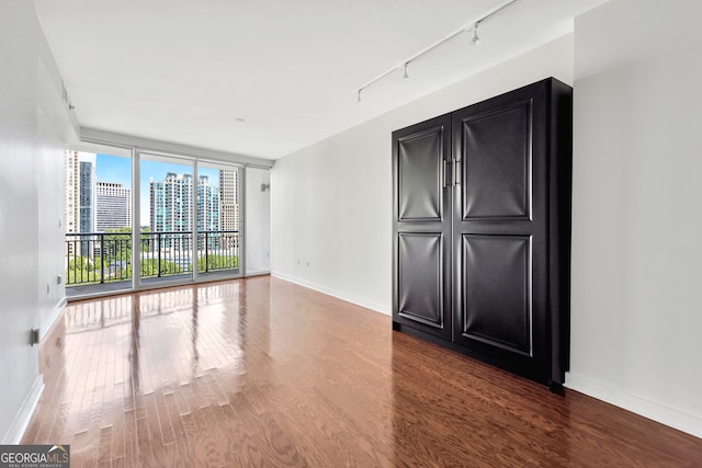 spare room with track lighting, a wall of windows, and hardwood / wood-style floors