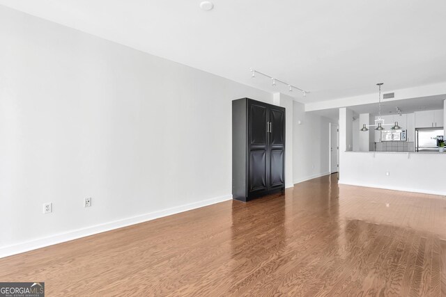 unfurnished living room with hardwood / wood-style floors, a notable chandelier, and track lighting