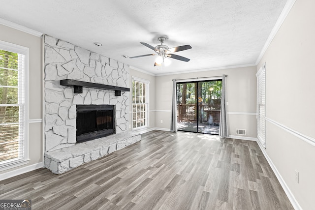 unfurnished living room featuring hardwood / wood-style floors, crown molding, a textured ceiling, ceiling fan, and a stone fireplace