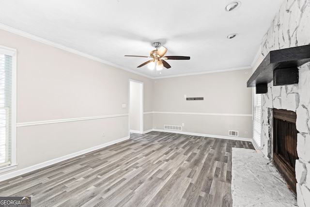 unfurnished living room featuring ceiling fan, hardwood / wood-style floors, a large fireplace, and a healthy amount of sunlight