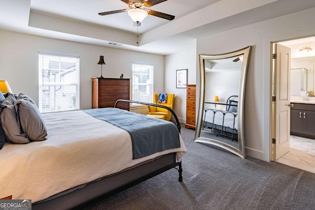 bedroom featuring ceiling fan, connected bathroom, light colored carpet, and a raised ceiling