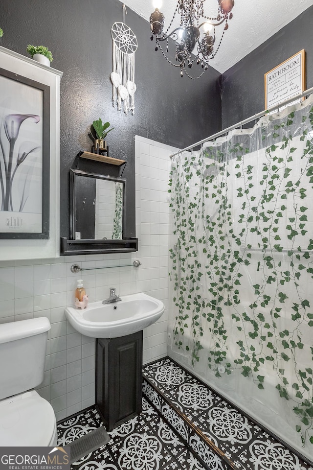 full bathroom with curtained shower, tile patterned flooring, toilet, tile walls, and an inviting chandelier