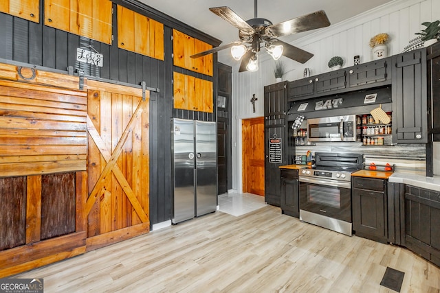 kitchen with a barn door, light wood-style flooring, a ceiling fan, light countertops, and appliances with stainless steel finishes